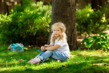 Fototapeta premium School girl listening book in park. Concept of distance learning.