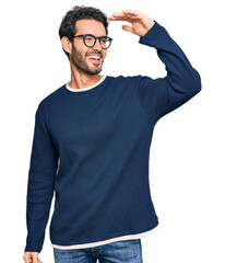 Young hispanic man wearing casual clothes and glasses very happy and smiling looking far away with...