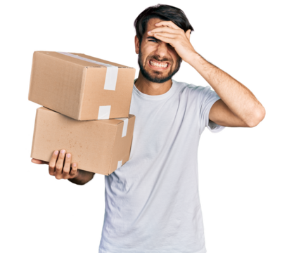 Hispanic man with blue eyes holding packages stressed and frustrated with hand on head, surprised and angry face - Powered by Adobe