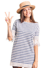 Obraz na płótnie Canvas Beautiful caucasian woman wearing summer hat showing and pointing up with fingers number three while smiling confident and happy.