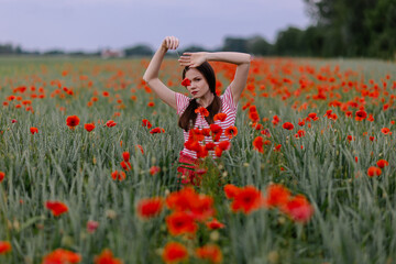 A beautiful woman stands in a poppy field and smiles portrait. Red flower. Beautiful flowering in nature. Poppy flower. Red dress. Out of town freedom outdoor