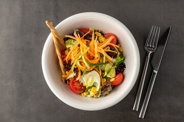 Salad with carrots, tomatoes, corn and lots of greens on a white porcelain plate