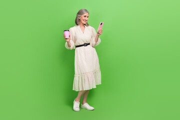 Full length photo of pretty sweet lady wear beige dress drinking beverage chatting instagram twitter telegram isolated green color background