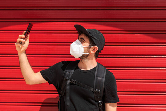 Man in mask taking photo on smartphone on red background