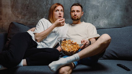 A couple in love eating popcorn sitting at home and watching TV