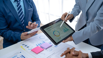 Business team together to make investment planning on digital tablet at the meeting. Close-up of a business consultant pointing to graphs and charts analyzing company growth.