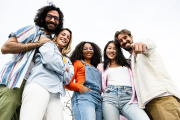 Low view of confident multiracial group of young hipsters laughing and pointing and looking at camera. Happy diverse group of young hipsters staring at camera outside 
