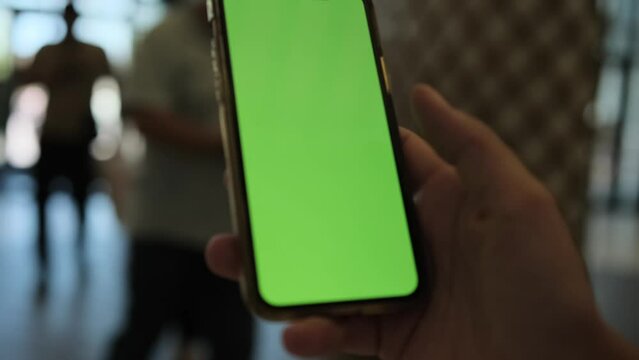 Female slides green chromakey screen on smartphone device with fingers, blurred background. Human enjoy online chat, internet purchase, browse web, download new cool freeware application. 