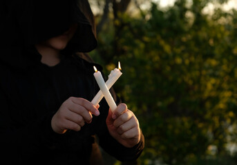 dress black witch with burning candles in hands close up, blurred dark natural background. sign of...