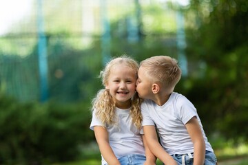 Beautiful little girl kissing his friend on natural park background.