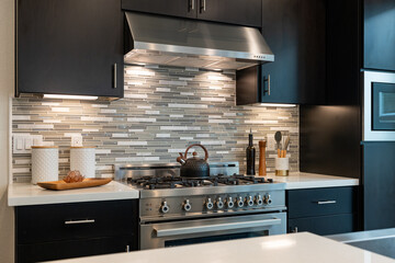 Modern kitchen details of large gas stove, black cabinetry and horizontal gray tile backsplash.