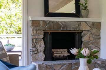 Living room detail of stone fireplace with blue and birch logs and view to outside.