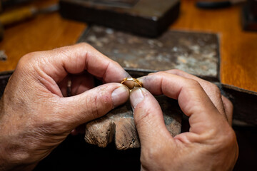 Goldsmith man working in his crafting jewelry workshop repairing and creating a gold ring with a...