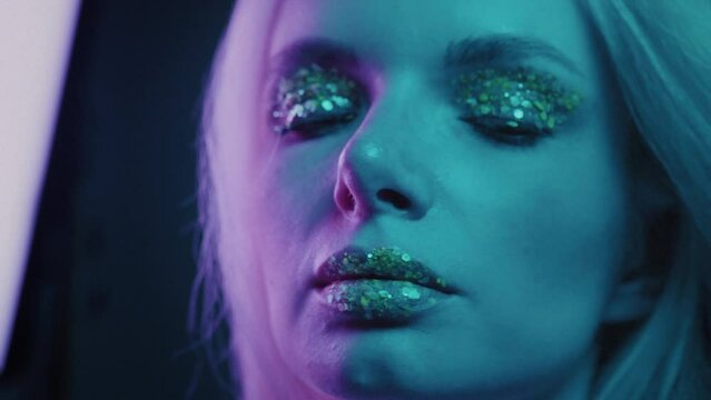 Close up is a beautiful blonde girl in a neon studio, dressed in a shirt. Beauty portrait of a woman's face. Female with plum lipstick. Clean skin, glitter with lips and eyes. Neon light in the club