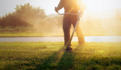 Close-up shot of municipal worker holding a lawnmower, trimming the grass in a public park during a...