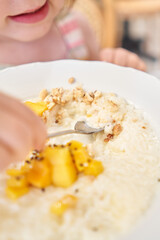 Little kid having breakfast at cafe. Adorable girl drinking still water, eating rice porridge with mango. enjoying breakfast. 