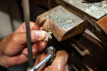 Goldsmith jeweler man working in his crafting jewelry workshop creating and sawing a white gold or silver jewel in his work studio. Jewel, craft and luxury concept.