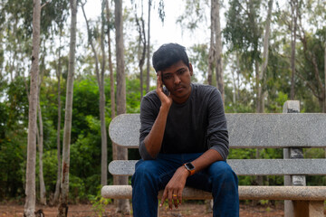 Fototapeta premium A portrait of a depressed Indian man sitting on a bench in a park.