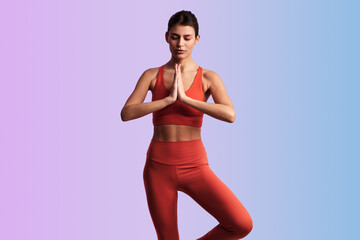 Calm woman meditating in tree pose with namaste hands in studio
