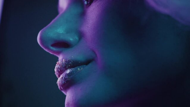 Extreme close up a beautiful blonde girl in a neon studio, sexually opens eyes and mouth. Beauty portrait of a woman face. Female with beautiful make up, glitter shadows and false lashes. Neon light