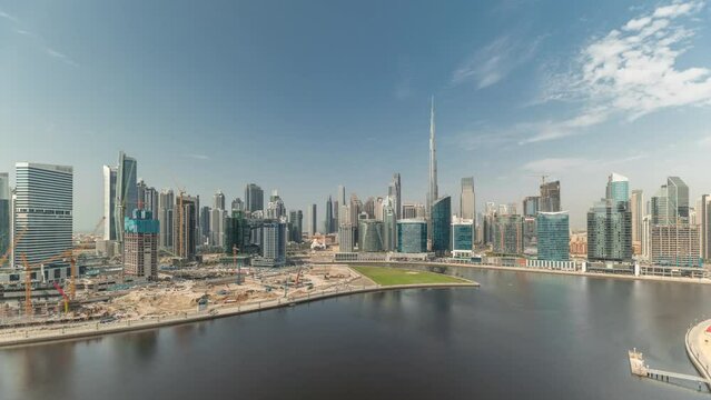Panorama showing aerial view to Dubai Business Bay and Downtown with the various skyscrapers and towers along waterfront on canal timelapse. Big construction site with cranes