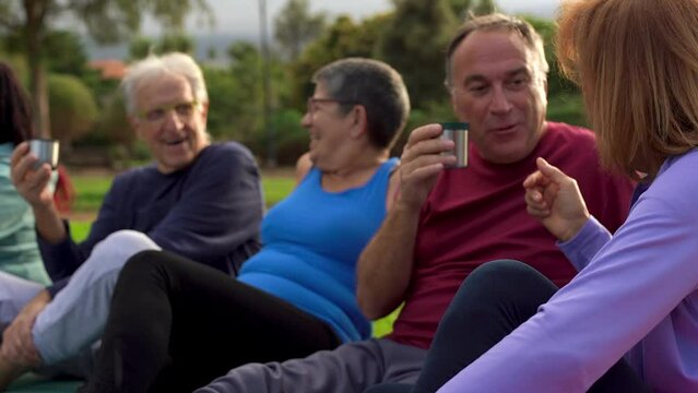 Happy senior people having fun together at park after yoga class - Elderly friends drinking hot tea outdoor