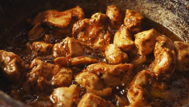 Chunks of chicken in spices fried in a cast-iron skillet in oil gurgle. Close-up