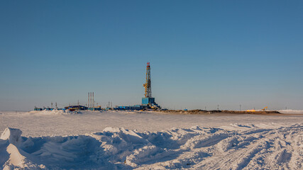 A gas field in the Arctic. Polar winter day. In the foreground is a snowy tundra. In the background is a drilling rig and industrial infrastructure