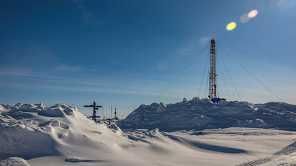 The Northern gas field. There is a lot of snow in the foreground. In the background is a mobile installation for well repair. A frosty winter day. Sunny blue sky