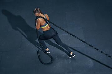 Female athlete fitness rope pull training. Sporty sportswoman working out in functional training...