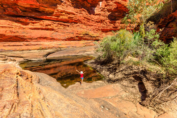 Permanent waterhole in Garden of Eden reflecting sandstone walls of Kings Canyon, Watarrka National Park. Woman with hat enjoys natural pool.Trekking in Australia Outback Red Center Northern Territory