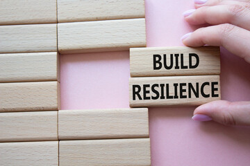 Build resilience symbol. Wooden blocks with words Build resilience. Beautiful pink background....