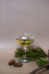 A glass of champagne surrounded by fir branches and cones on a beige background. Cocktail for the New Year. For the design of cards, invitations, posters, illustrations, presentations, flyers.