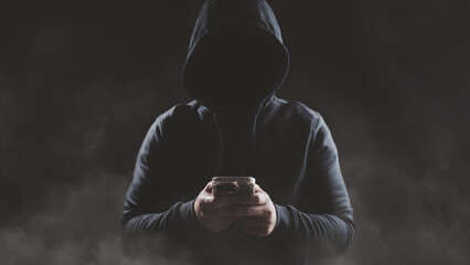 Hacker wear hood holding smartphone with red warning icon to launch ransomware malware attack on victim. Cyber security protection and hacking concept.