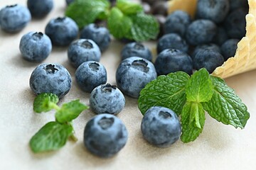 ripe blueberries spilled out of a waffle cup on a table with a green mint leaf
