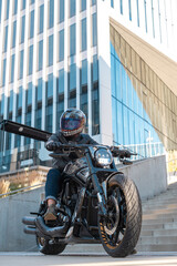 Handsome motorcyclist with helmet sitting on his moto against urban backdrop