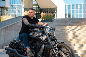 Handsome biker without helmet sitting on his moto against urban background