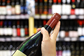 Wine bottle in female hand, customer in liquor store. Woman choosing and buying alcohol