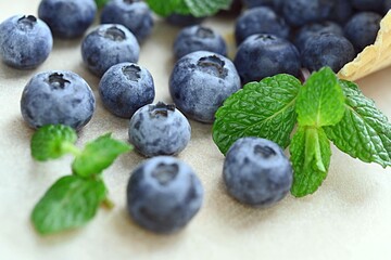 ripe blueberries spilled out of a waffle cup on a table with a green mint leaf