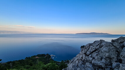 Panoramic view of the shore along Medveja, Croatia seen from above. The town is surrounded by thick forest. The sky has colors of sunrise. Endless horizon. An island in the back. Summer holidays