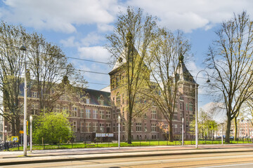an old brick building in the middle part of amsterdam, with trees lining the street and cars parked on the side