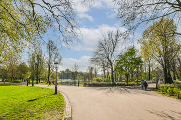 a park with trees, grass and people walking along the path on a sunny day in springtime stock photo