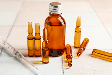 Medical ampules, bottle and syringe on white tile background