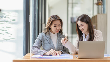 Two asian businesswoman sitting and consulting business inside modern office discussing presentation of startup project idea Analyze statistics and investment markets at the office.