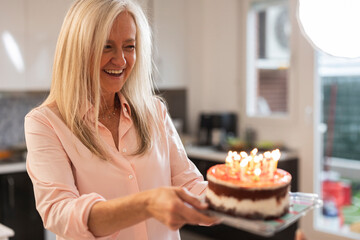 happy senior woman with gray hair carrying a birthday cake with candles
