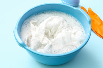 Plastic basin with dirty clothes, water and foam on blue background