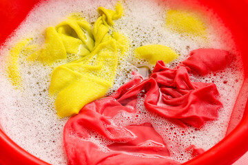Plastic basin with dirty laundry, water and foam, closeup