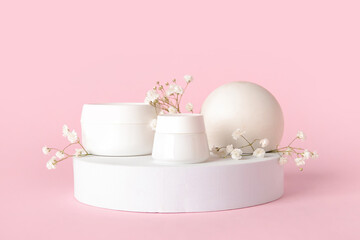 Composition with jars of cosmetic products, plaster podiums and gypsophila flowers on pink background