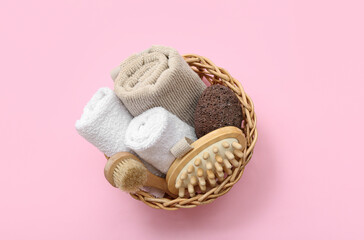 Fototapeta na wymiar Wicker basket with clean towels, massage brushes and pumice stone on pink background