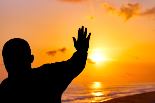 A mesmerizing image of a man standing in prayer, his figure highlighted by the beautiful solstice sunset, symbolizing his faith and devotion to Jesus.